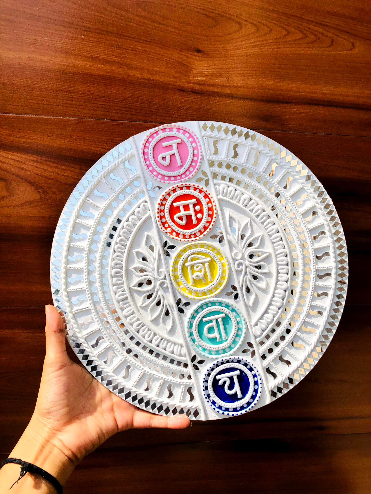 Handcrafted colorful Lippan Mud and Mirror artwork with Hindi lettering, held by a hand